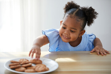 African child girl picking and eating chocolate cookies or biscuits from dish
