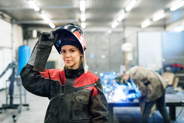 Beautiful blonde woman works as a welder in workshop, operating welding machine, wearing protective...
