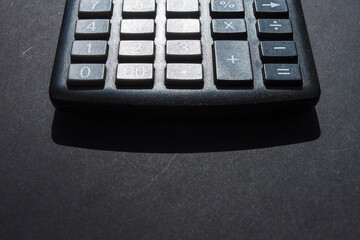 A fragment of a calculator on a dark background. Sunlight.  With blank space for a text. Copy space