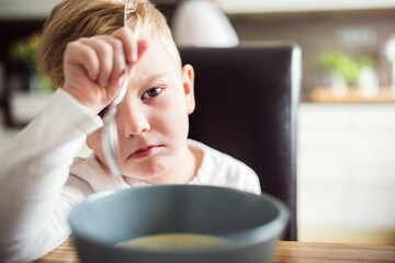 Little boy doesn't like lunch, doesn't want to eat. Sitting at table with serious expression,...