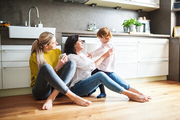 Mother, grandmother and little granddaughter in kitchen, sitting on floor. Family time, three...