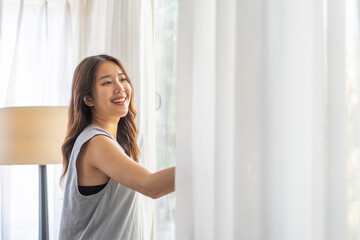 Happy young beautiful pretty asian woman waking up and opening window curtains.Girl feeling...