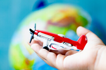 Child's hand holding a toy airplane with a propeller in his palm. Red toy plane in front of world...