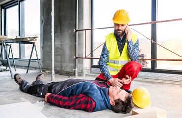 Colleague giving first aid to unconscious worker after accident, calling ambulance. Concept of...