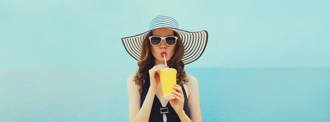 Summer portrait of beautiful young woman drinking juice wearing swimsuit, hat on the beach at sea