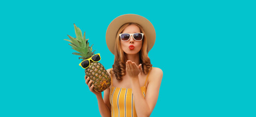 Summer portrait of beautiful young woman blowing a kiss posing with pineapple wearing hat, glasses
