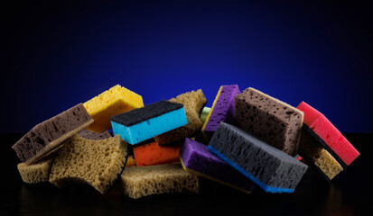 Background of mixed colorful sponges for washing dishes. Household cleaning sponge on a blue...