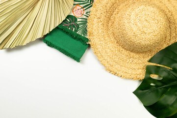 Top view of straw hat, dried palm leaf, green towels and monstera leaf on white background. Summer...