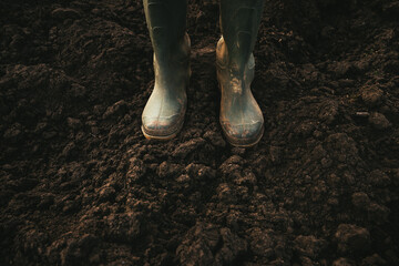 Agronomist standing on tilled soil ground, closeup of rubber boots