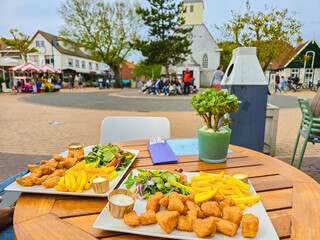 Two beautifully arranged plates of food sit on a table in the bustling town square of Texel,...