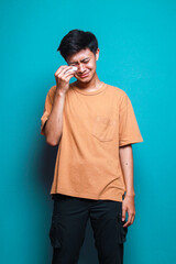 Young man crying and using tissue to rub the tears isolated on teal background
