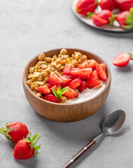 Natural yogurt with granola and strawberries in a wooden bowl on a blue background with fresh berries.