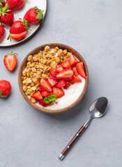 Natural yogurt with granola and strawberries in a wooden bowl on a blue background with fresh berries.