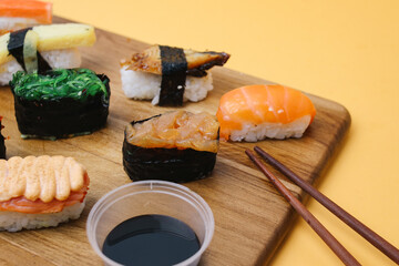 Sushi platter. A selection of raw fish and rice snacks with chopsticks on yellow background.
