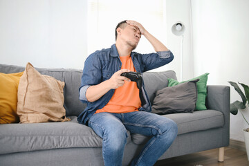 Unhappy Asian man loose in video game, playing with joystick at living room
