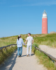 A couple strolls hand in hand on a winding path, gazing out at the iconic lighthouse along the...