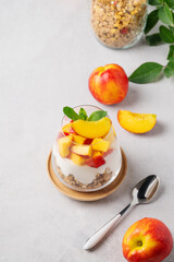 Flat lay of greek yogurt parfait with peach and muesli in a glass on a light background with fresh fruits and spoon. Healthy eating concept.