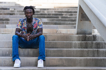 Low angle full body of serious African American male in colorful shirt and jeans with sneakers...