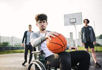 Disabled young man in a wheelchair playing basketball with his friends. Teamwrok and male...
