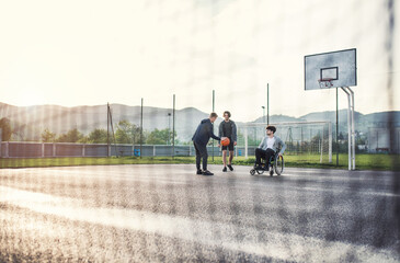 Disabled young man in a wheelchair playing basketball with his friends. Teamwrok and male friendship.