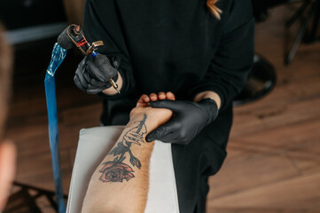 Close up tattoo master  professional tattoo artist in black gloves making a  rose tattoo on a man's...