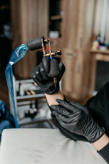 Woman professional tattoo artist in black gloves holding  a tattoo machine.