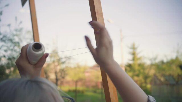 a woman ties ropes around a frame for a grape bush.