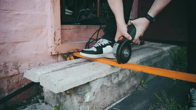 A man saws a thin board with a grinder. on the threshold of his workshop.