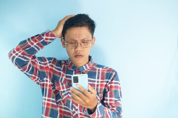 Young Asian man looking at mobile phone with sad expression while holding head