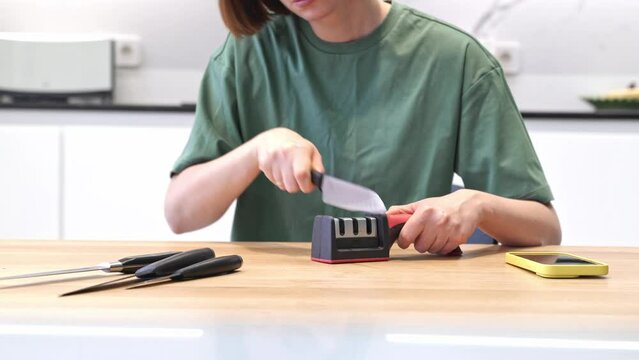 Close-up of woman sharpening knife with special knife sharpener at home	