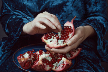 Person delicately separating pomegranate seeds over a blue velvet backdrop. Close-up shot with rich...