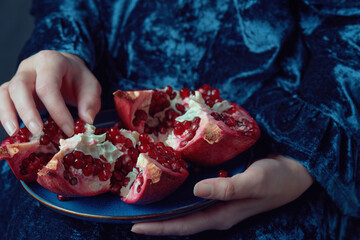 Hands holding a fresh pomegranate on a blue plate. Close-up shot with rich colors and textures....