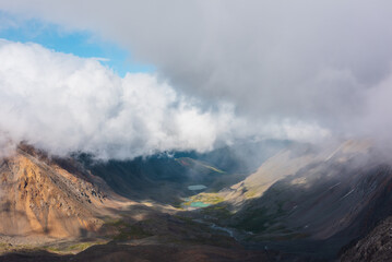 Aerial top view to green rocky hilly valley with two turquoise lakes under lush low clouds. Most...
