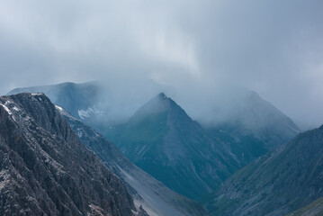 Atmospheric landscape with rocky peaked mountain top of triangle shape in low rainy cloud. Dramatic view to pointy pyramid shaped peak in rain time. Sheer crags and sharp pinnacle in gray cloudy sky.