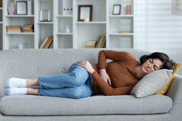 Fototapeta premium Woman in pain lying on a couch holding her stomach at home