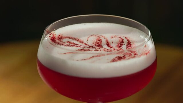Close up of champagne saucer glass filled with clover club cocktail decorated with hibiscus powder poured in floral pattern. Long two layered drink with adding of gin and intense raspberry flavour.