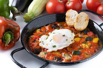 Vegetable pisto manchego with tomatoes, zucchini, peppers, onions,eggplant and egg, served in frying pan isolated on white background