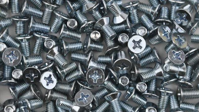 A scattered of metric countersunk M6 threaded bolts. Movement with rotation. Close-up, flat lay, top view.