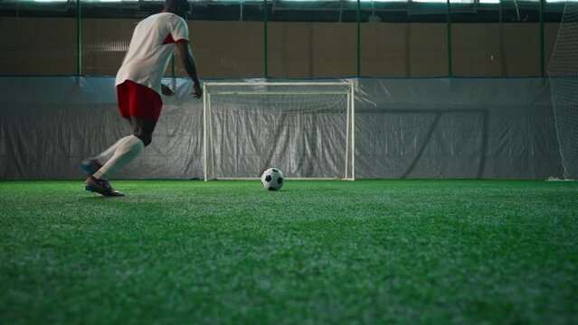 Black soccer player exercising penalty in training hall, scoring goal, back view