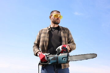Man with modern saw against blue sky, low angle view