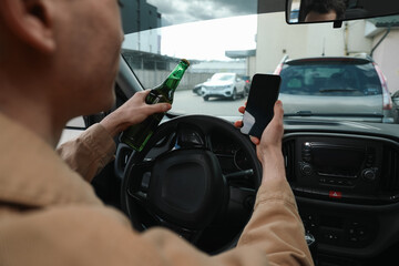 Man with bottle of beer and smartphone in car, closeup. Don't drink and drive concept