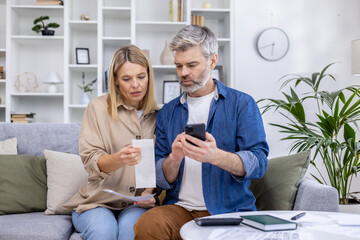 Middle-aged couple managing finances and reviewing household bills together at home while...