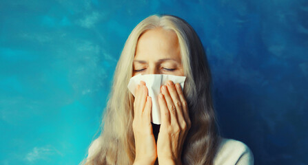 Sick exhausted mature woman sneezing blow nose using tissue at home