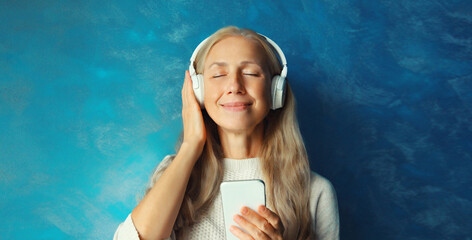 Portrait of happy smiling caucasian mature woman listening to music in headphones with smartphone