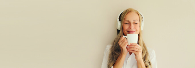 Portrait of happy relaxed middle aged woman listening to music drinking coffee in headphones