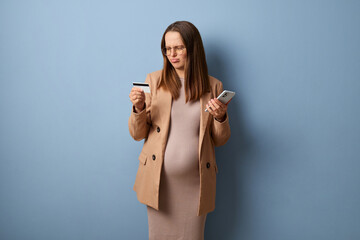 Confused sad upset disappointed pregnant woman wearing dress and jacket isolated over blue...