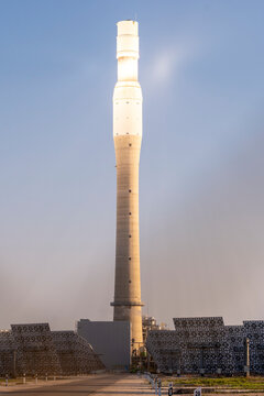 A dramatic image of a concentrated solar power plant tower with the sun's reflection under a clear sky during sunrise or sunset