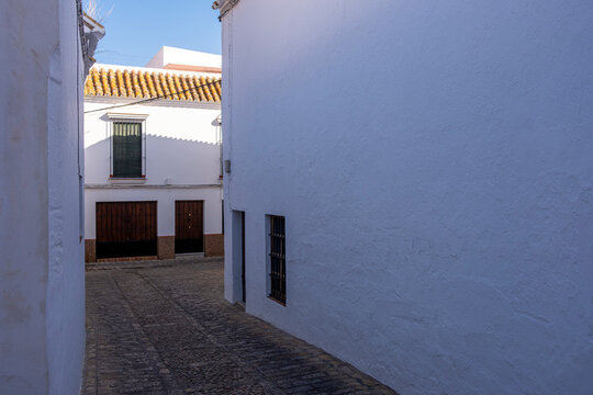 The contrasting shadows play across the facade of a traditional whitewashed building in a cobblestone street of Carmona, Andalusia, Spain