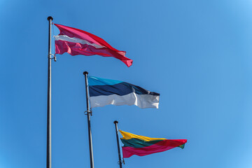 Latvian, Estonian and Lithuanian flags on flagpoles against blue clear sky