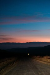 Fototapeta premium Dirt road with a mountain range in the background at sunset.